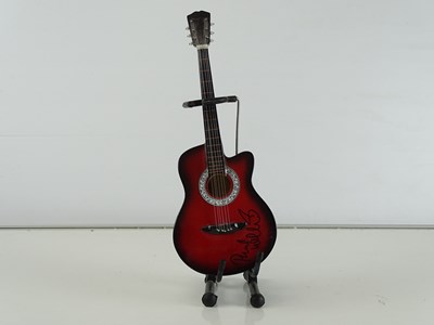 Lot 127 - A mini model guitar with stand signed to the...
